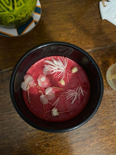 Pink candle and white flowers in a black jar resting on a wooden base