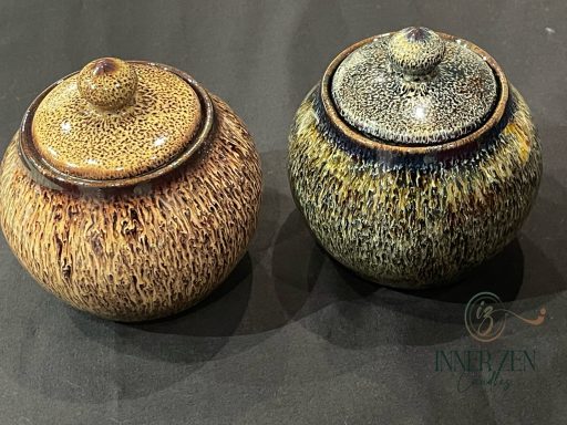 Two decorative ceramic jars with textured surfaces and lidded tops, one brown and one blue.