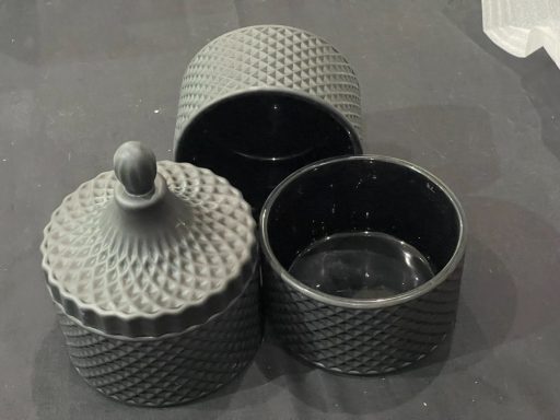 Two textured, black storage containers with lids, one partially open.