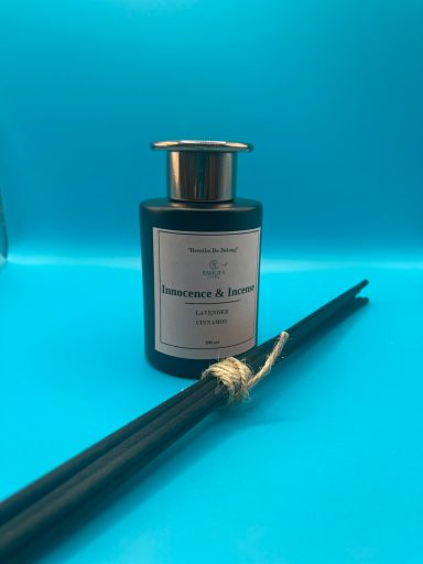 Black diffuser bottle with a gold cap and bamboo sticks against a blue background.