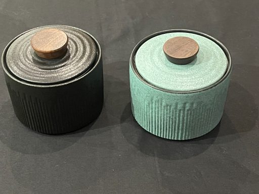 Two decorative containers, one black and one teal, with wooden lids.