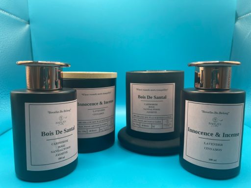 Four black containers with metallic lids, labeled as scented candles, on a blue background.