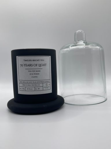 A black candle jar with a label and a clear glass dome cover beside it.