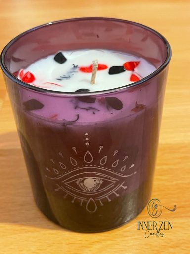 A purple candle with decorative red and black elements in a glass holder.