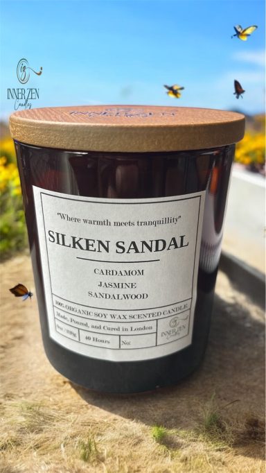 Jar of Silken Sandal fragrance in a scenic outdoor setting with flowers and butterflies.