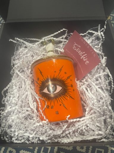 Orange bottle with an eye design, displayed in a box with crinkled paper.