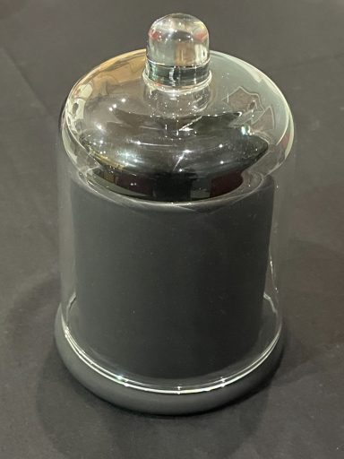 A transparent glass cloche covering a black cylindrical object.