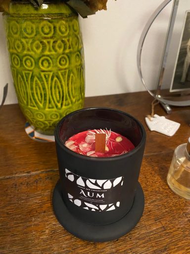 A black candle holder with decorative text, containing a red candle and a stick on top.